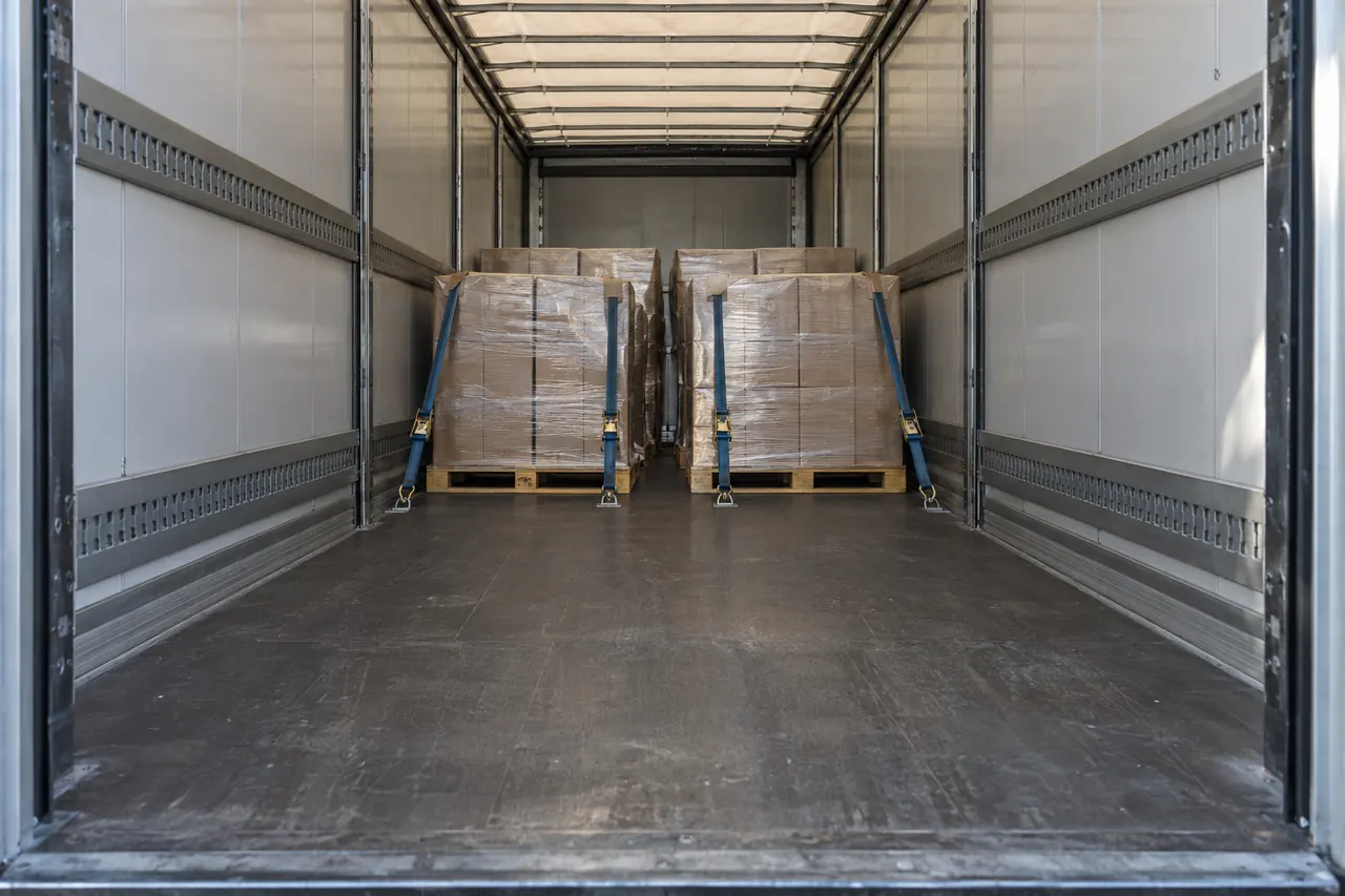Palets bien trincados en el interior de un tráiler cargado a medias, con la luz entrando por las puertas abiertas.